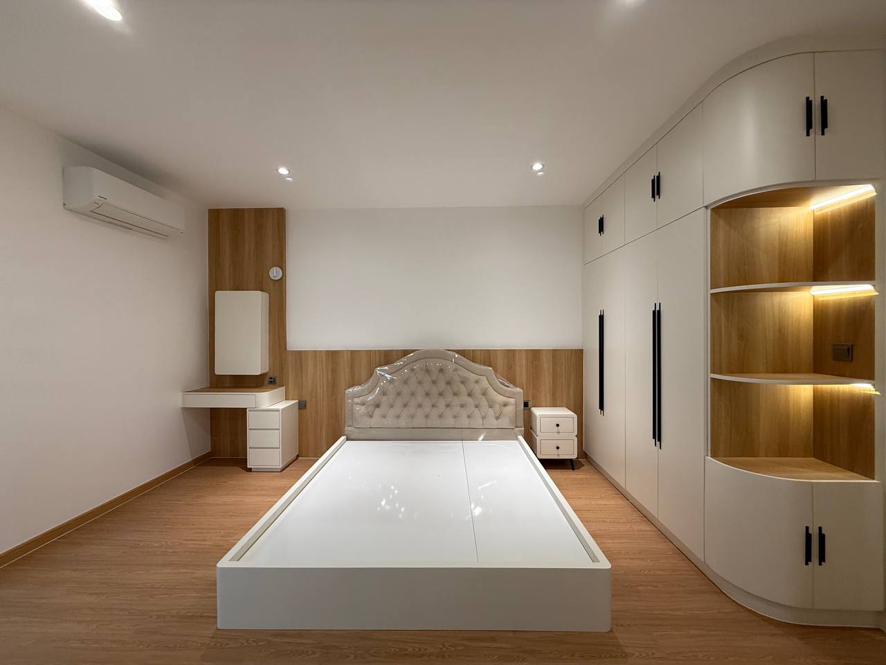 Villa bedroom with upholstered bed, white fitted wardrobe, warm wood wall panels and illuminated display niche