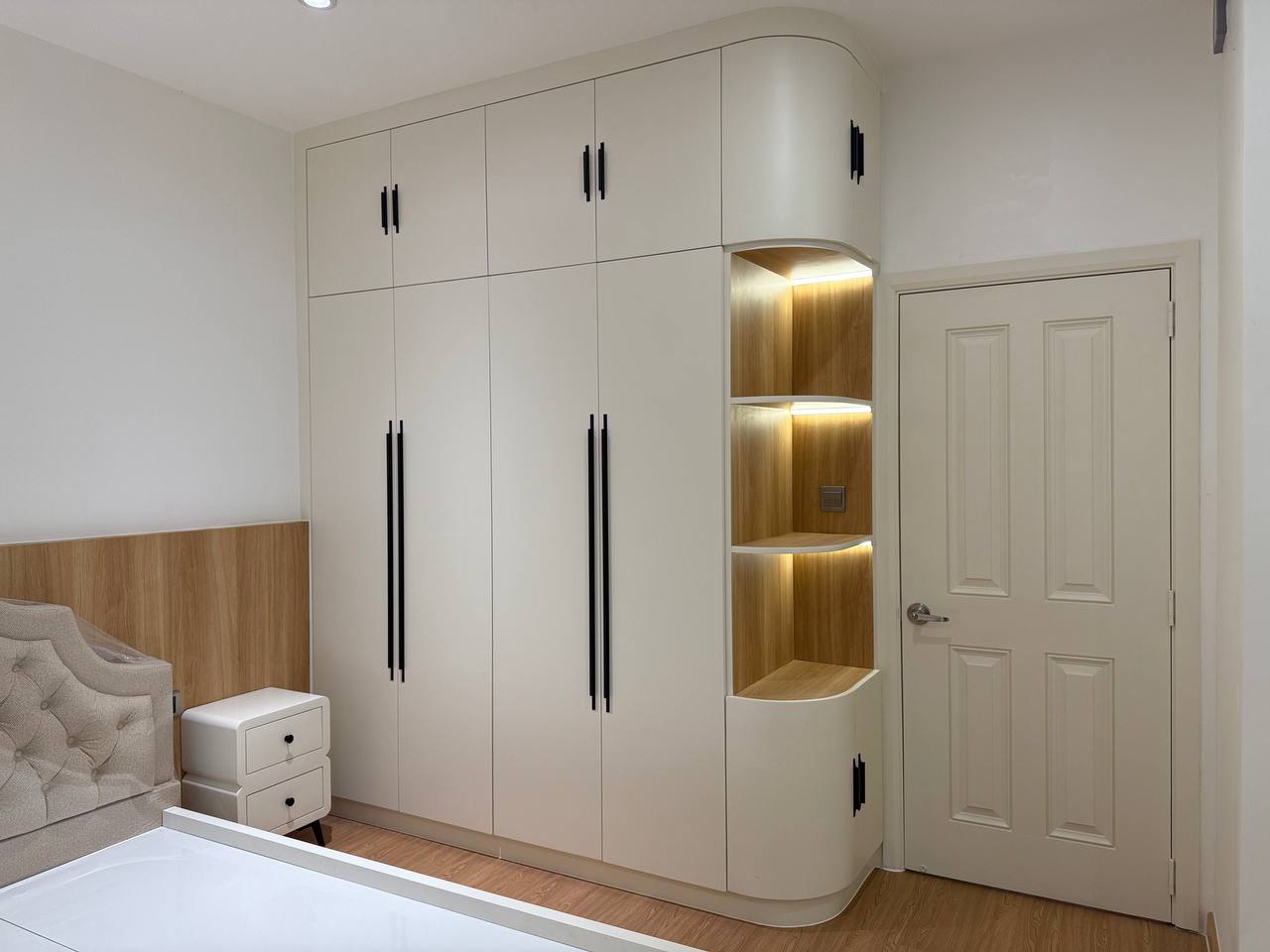 Bedroom wardrobe with curved end and lit display niche beside the bed