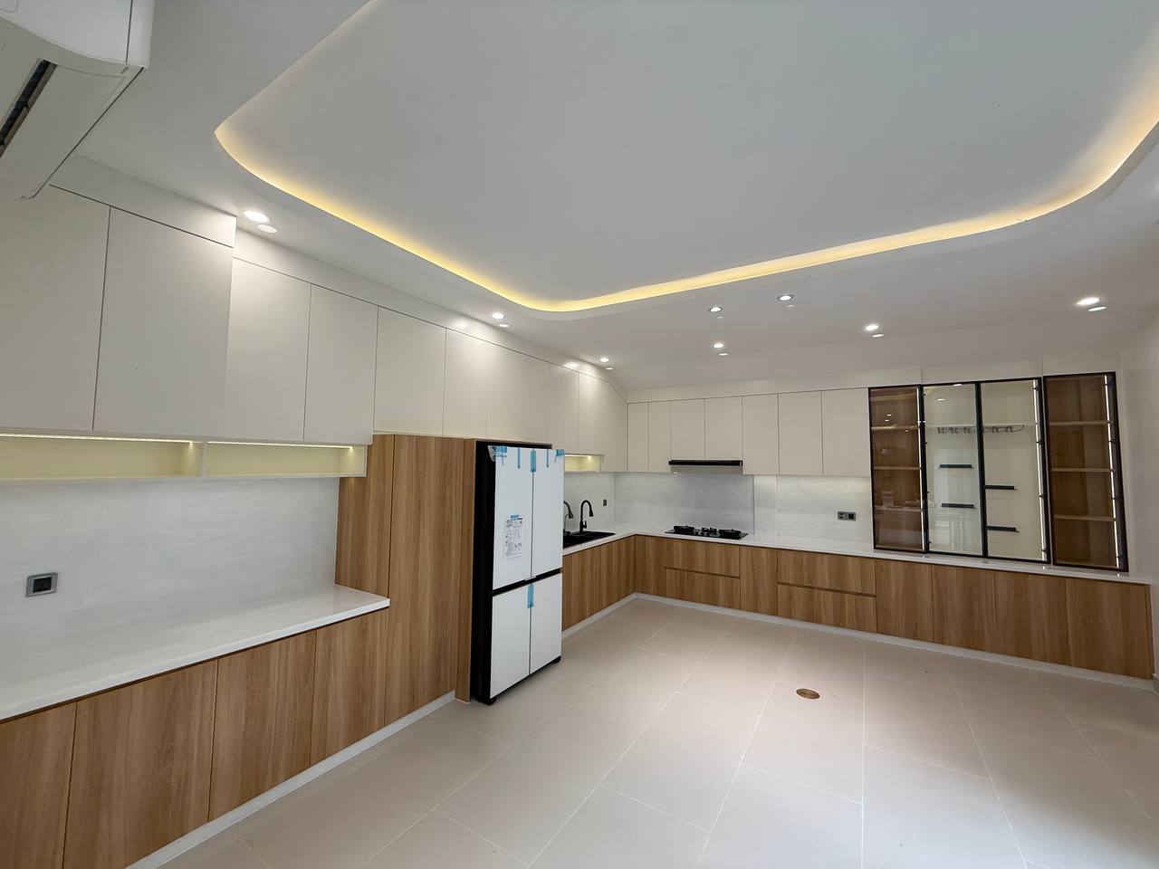 Wide kitchen with white upper cabinets, wood-toned lower cabinets and bright work surfaces
